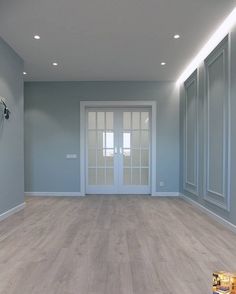 an empty room with light blue walls and wooden floors, white trimmings on the doors