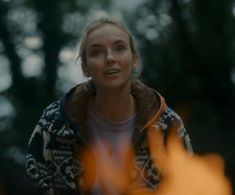 a woman standing in front of a fire with her eyes wide open and looking at the camera