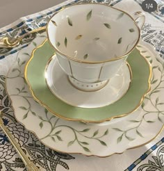 a white and green tea cup sitting on top of a plate next to a fork