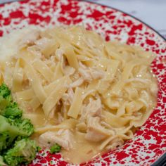 a red and white plate topped with pasta, broccoli and meat covered in gravy