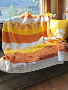 an orange and white crocheted blanket sitting on top of a couch next to a window