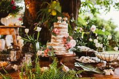 a wedding cake sitting on top of a wooden table surrounded by flowers and greenery