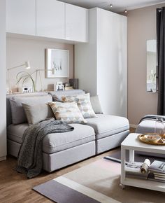 a living room filled with furniture and pillows on top of a wooden floor next to a window