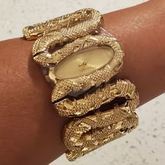 100% Authentic Poshmark Will Authenticate Over $500 Roberto Cavalli Cleopatra Women's Gold Tone Snake Bracelet Watch New With Tags, Includes Box Brushed Gold Tone Oval Analog Face Polished Gold Tone Snake Form Hour And Minute Hands Roberto Cavalli Logo At The 12 O'clock Position Gold Tone Stainless Steel Fixed Bezel Stainless Steel Case Back Polished Gold Tone Raised Texture Stainless Steel Bangle Style Watch Band Push Action Inset Closures Fast Shipping! New To Poshmark? Use Referral Code Mibel High Jewelry Gold, Gold Bangles Black Women, Roberto Cavalli Jewelry, Gold Wire Wrapped Jewelry, Unique Bracelet Design For Women, West African Jewelry, Gold Snake Bracelet, Gold Earthy Jewelry, Stacked Watches