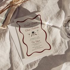 a wedding card and wine glass sitting on top of a white cloth covered tablecloth