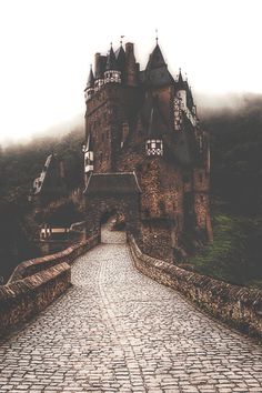 an old castle with cobblestone walkway leading into the foggy area behind it