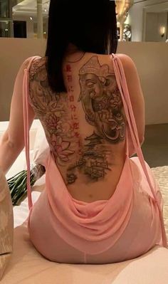 a woman sitting on top of a bed with tattoos on her back and arms behind her