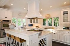 a large kitchen with white cabinets and marble counter tops, two stools at the island