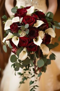 a bridal holding a bouquet of red roses and calla lilies in her hands