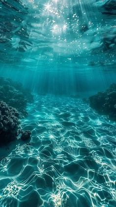 an underwater view of the ocean with sunlight coming through the water and rocks in the foreground