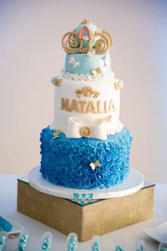 a three tiered blue and white cake on top of a gold plated box