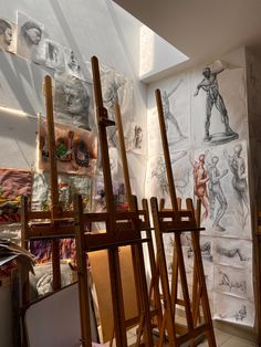 an artist's studio with several wooden easels and drawings on the wall behind them