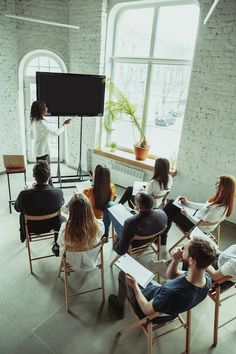 a group of people sitting around each other in chairs watching a woman giving a presentation