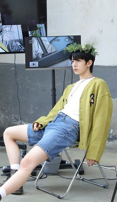 a young man sitting in a chair with his legs crossed and wearing a green cardigan