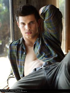 a young man leaning against a window with his shirt off and looking at the camera