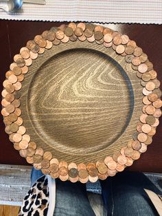 a wooden plate with coins on it sitting on someone's lap in front of a table