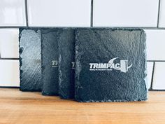 two black stone coasters sitting on top of a wooden table next to a tiled wall