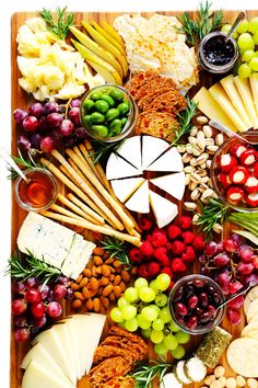 an assortment of cheeses, fruits and nuts arranged on a wooden platter with olives