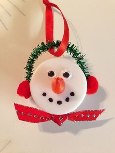 a snowman ornament hanging from a red ribbon on a white table top