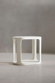 a white vase sitting on top of a table next to a gray wall and floor