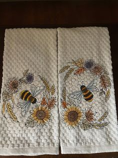 two white towels with bees and sunflowers on them, sitting on a table