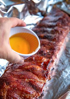 a person dipping sauce on top of a piece of meat in a tin foil container