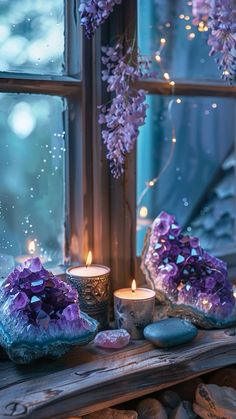 some rocks and candles are on a window sill with purple flowers in the background