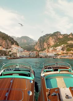 there are many boats in the water with buildings on the shore behind them and seagulls flying overhead