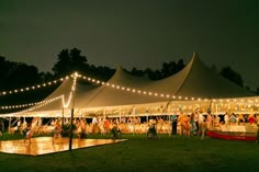 a group of people standing around a tent at night with lights on the roof and in the water