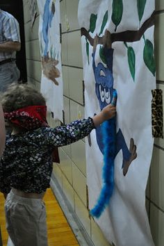 a young boy is painting on the wall with blue paint and another child is reaching for it