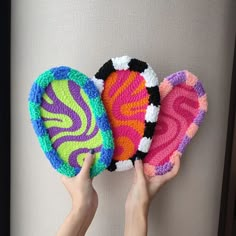 two hands are holding three colorful crocheted objects