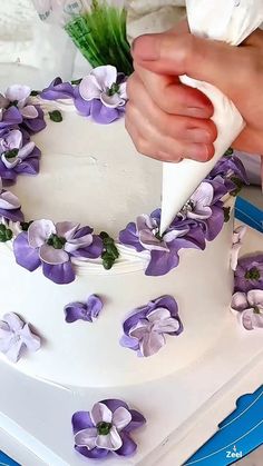 a person is decorating a cake with purple flowers