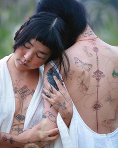 two women with tattoos on their back hugging each other