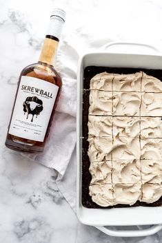 a cake in a pan with frosting next to a bottle of whiskey