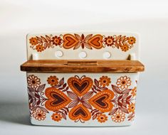 an orange and white flowered ceramic dish with wooden cutting board in front of it