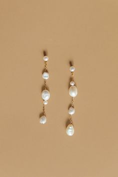 two pairs of earrings with pearls hanging from the end of each earring, on a beige background