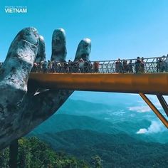 people are standing on a bridge above the mountains and trees with their hands raised up