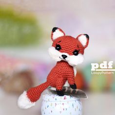 a crocheted red fox sitting on top of a white ball with sprinkles