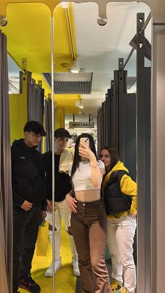 a woman taking a selfie in front of a mirror while three people look at her