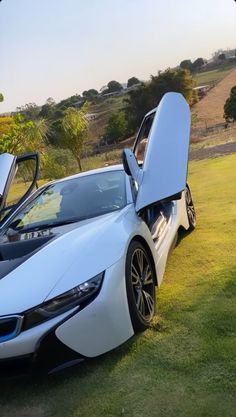 two white sports cars parked next to each other on a grass covered field with open doors