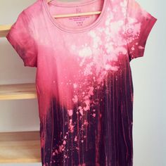 a t - shirt with pink paint splattered on it sitting on a rack