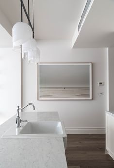 a white kitchen with marble counter tops and an island sink in front of a large mirror