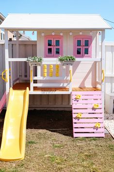 a toy house with a slide and flower boxes on the roof is painted pink, yellow and white