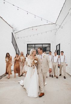 a bride and groom walking down the aisle with their wedding party in the back ground