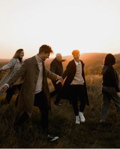 a group of people walking across a grass covered field next to each other at sunset