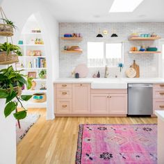 a kitchen with pink cabinets and wooden floors, an area rug in front of the sink