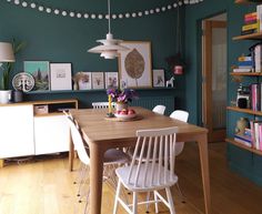 a dining room with green walls and wooden flooring, white chairs around a table