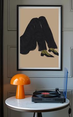 a table with a record player and an orange mushroom lamp on it in front of a painting