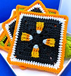 three crocheted coasters on a white plate with green and orange yarn around them