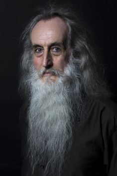 an old man with a long white beard and greying hair wearing a black shirt